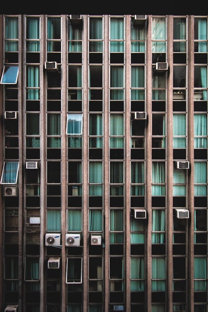 A modern building facade featuring vertical lines and air conditioners, contrasting with green tinted windows.