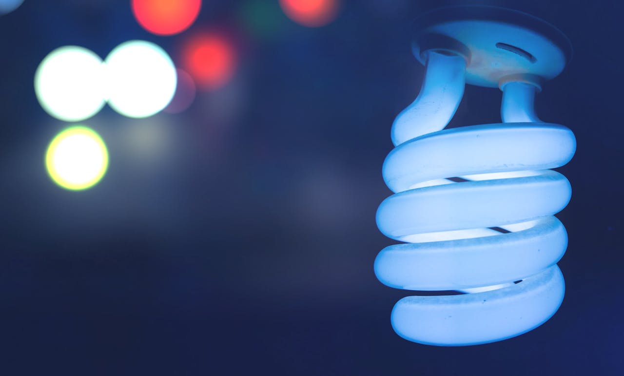 Illuminated spiral CFL bulb with colorful bokeh background, abstract lighting concept.